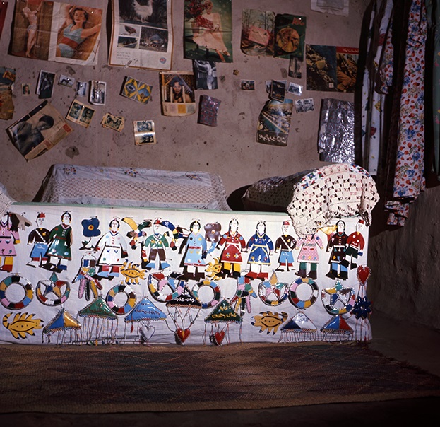 Bed coverlet decorated with small handmade objects. Magazine clippings and photos are displayed on the wall above the bed. Toshke, W. Neja Dukki Daur, 1964 (Photographed by the author).