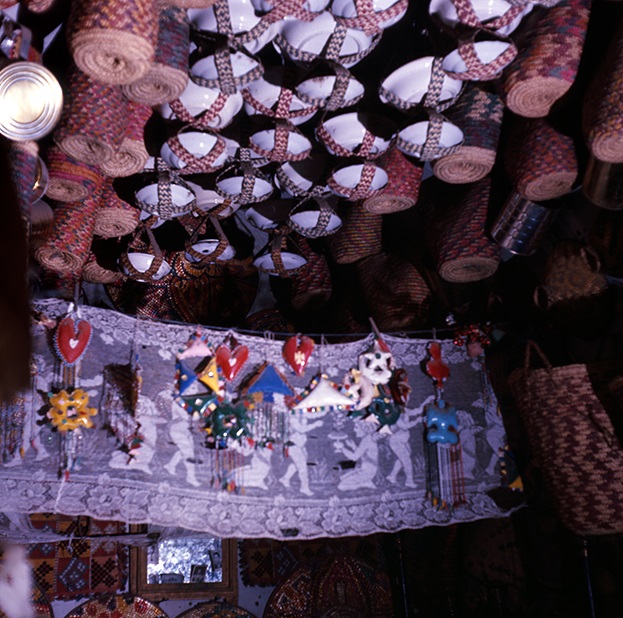 Enamel bowls in slings suspended from the ceiling, on the four posters a lace curtain to which protective small plastic objects are pinned. Shellaal, Bijje island, 1964 (Photographed by the author).