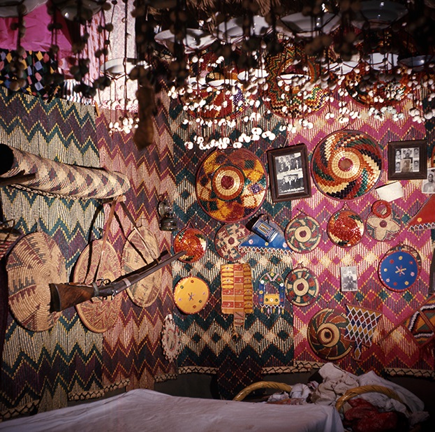 Bridal room with pleated mats, baskets, a gun, photos, and various small plastic objects, from the ceiling suspended slings with enamel bowls. Umbarakaab, W. Neja Siukutti, 1963 (Photographed by the author).